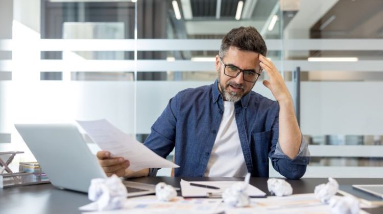 Frustrated Businessman Reviewing Documents At His Desk In A Modern Office