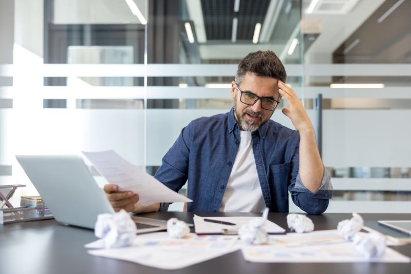 Frustrated Businessman Reviewing Documents At His Desk In A Modern Office