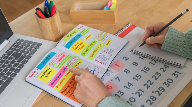 Business owner organising weekly priorities in a planner beside a laptop and calendar