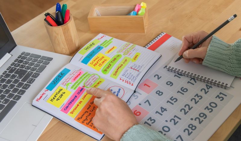 Business owner organising weekly priorities in a planner beside a laptop and calendar