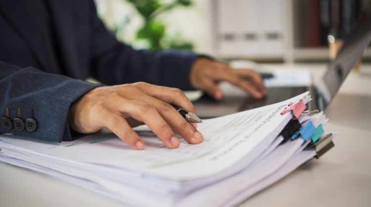 Business professional reviewing and organising printed documents beside a laptop
