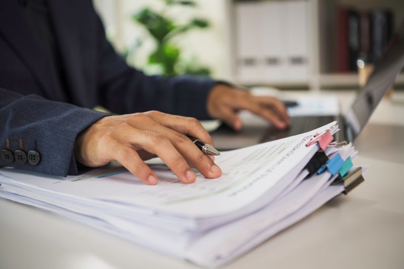 Business professional reviewing and organising printed documents beside a laptop