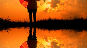 Child holding a parasol reflected in water