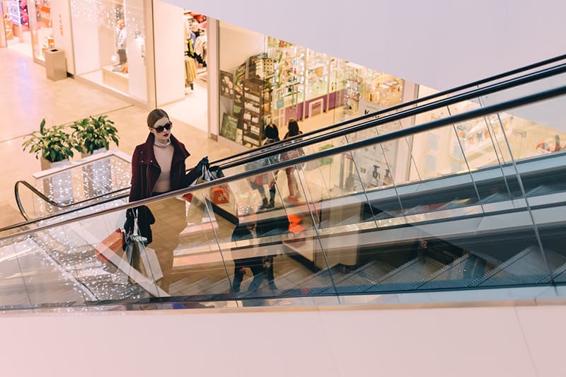 Woman carrying shopping bags riding escalator in retail shopping mall