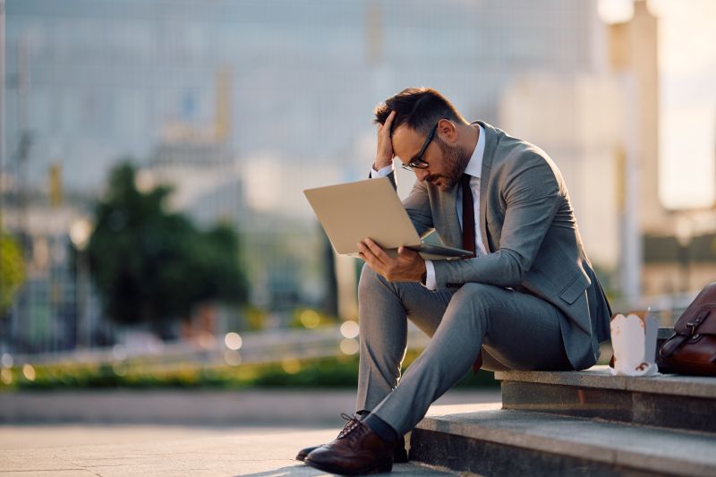 Stressed businessman using laptop in the city.