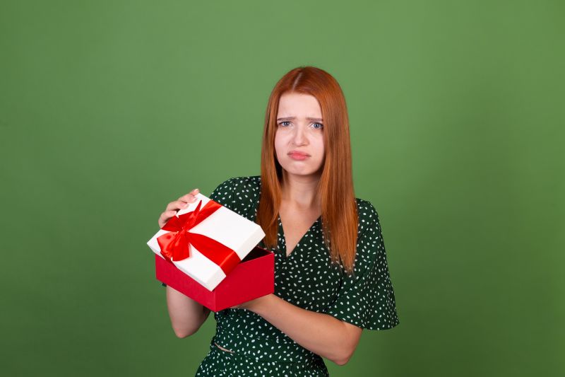 Young red hair woman on green background with gift box unhappy sad disappointed