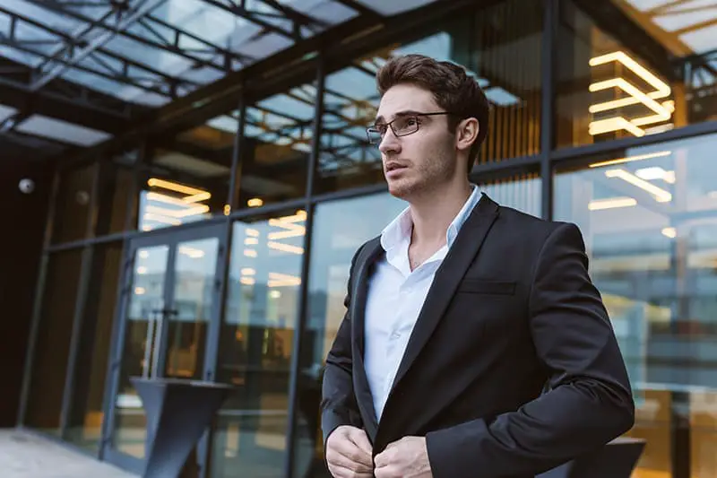 Business man in suit and glasses standing near the office. Side view