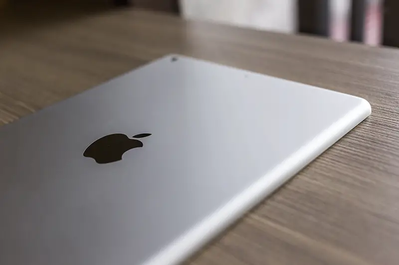 Logo of Apple in back Apple iPad air on wood desk.