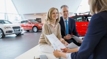 Saleswoman And Couple Finalizing Paperwork In Car Dealership
