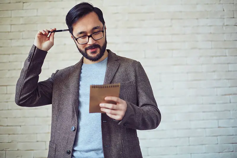 Male employee in eyeglasses looking at page of notepad