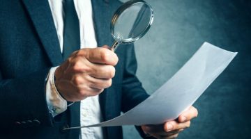 Man in suit looking at document through magnifying glass