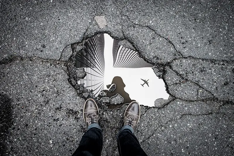 Person standing showing his reflection on the water on the ground