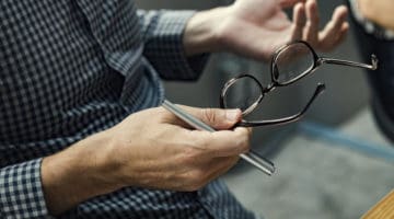 person holding pen and eyeglasses