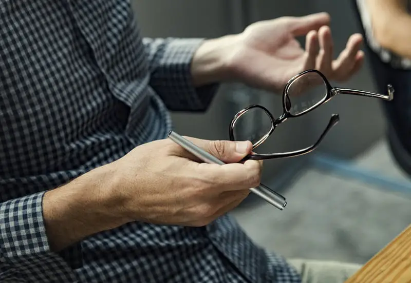 person holding pen and eyeglasses