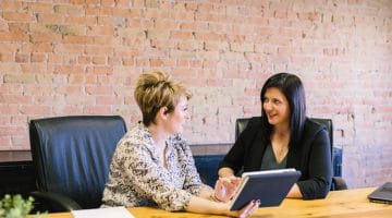 Two women having a discussion, one holding a tablet