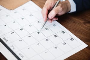 person pinpoint pen on calendar - Why Managing Employee Leave Properly Matters