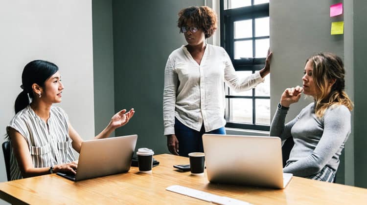 Team communication - three woment talking near laptop on desk in room