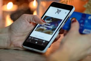 person using black and white smartphone and holding blue credit card for eCommerce checkout process