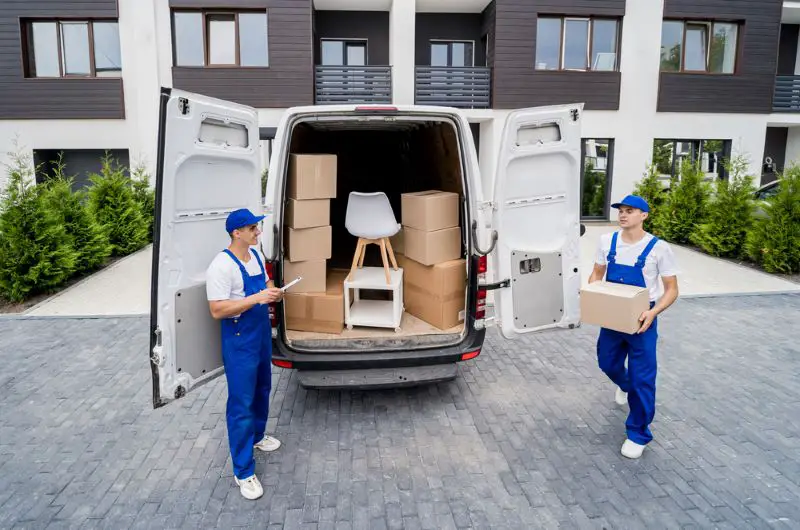 Two removal company workers are loading boxes into a minibus.