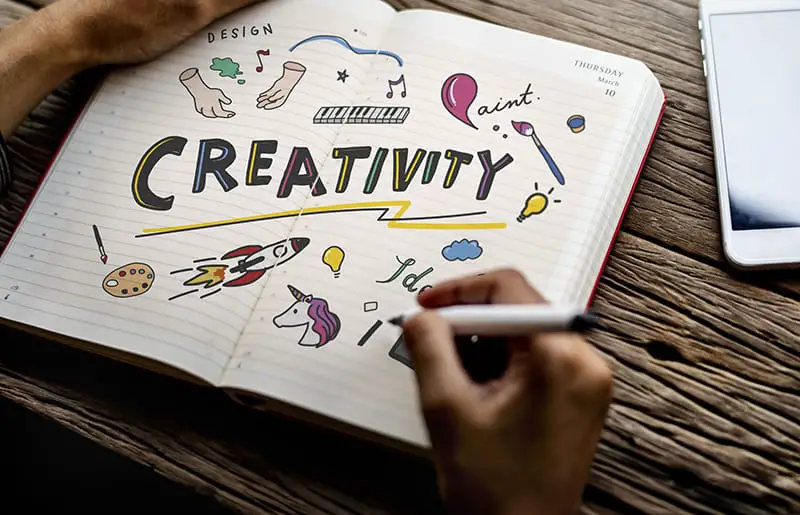 Person doodling pictures and the word “creativity” in a notebook.