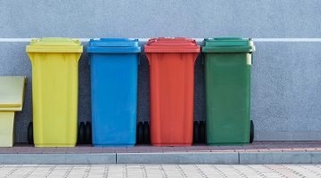 four assorted-color solid waste trash bins beside gray wall