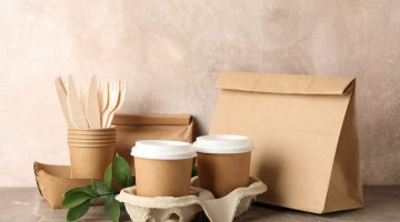Eco - friendly tableware and paper bag on grey tabl