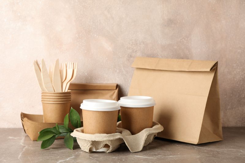 Eco - friendly tableware and paper bag on grey tabl
