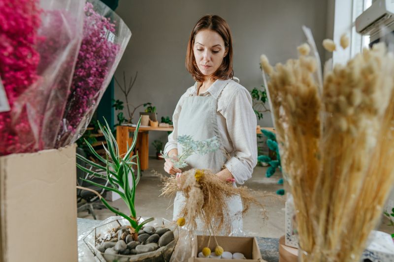 Young woman florist wearing apron making bouquet of dried flowers in the floral shop.