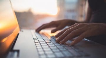 Woman typing on keyboard with sun reflecting off laptop screen