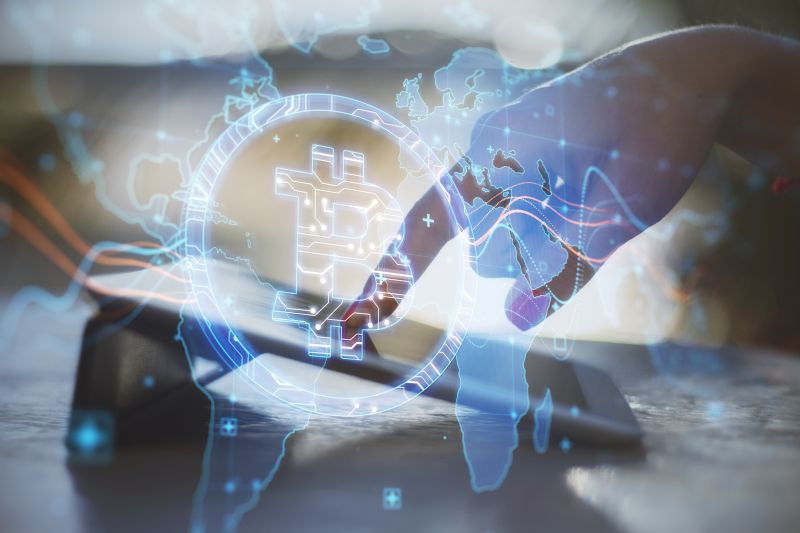 Close Up Of Hand At Desktop Using Tablet With Creative Glowing Global Bitcoin Hologram On Blurry