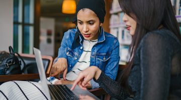 two women looking and pointing at macbook laptop