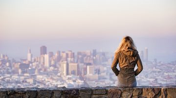 Woman on a rock wall looking out to urban environment - city