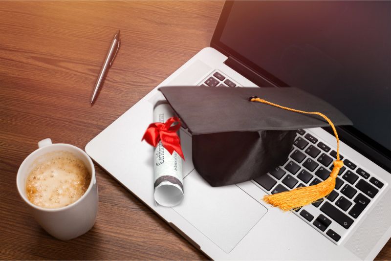 Laptop and diploma scroll and graduation hat
