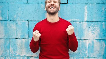 man wearing red long-sleeved t-shirt standing beside wall demonstrating personal power for success