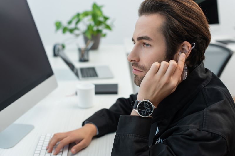 Man Working at Desk with Earpiece and Computer