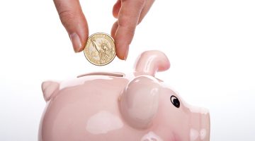 saving money – person putting dollar coin into piggy bank - investing