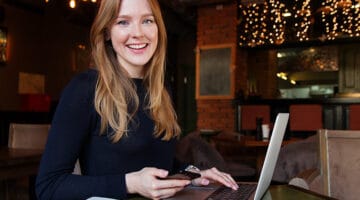 A young woman in fronrt of laptop while holding black smartphone