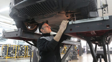 Man in black jacket working underneath a vehicle in car repair shop