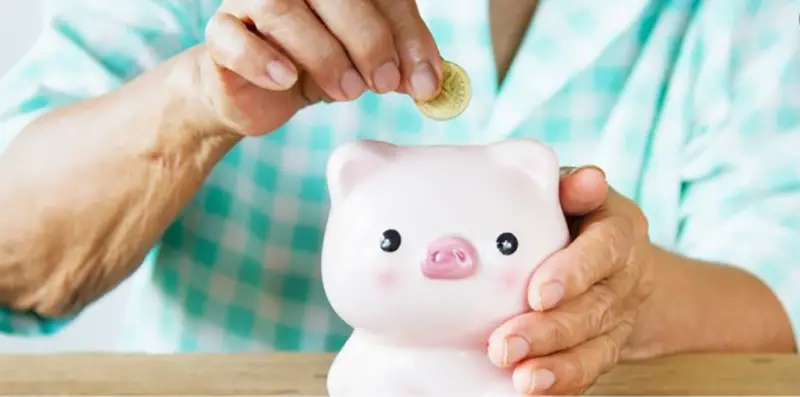 A person inserting a coin in a pink piggy bank