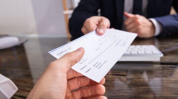 Close-up Of A Businessperson's Hand Giving Cheque To Colleague At Workplace