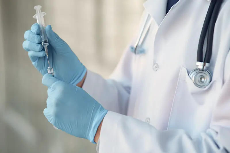 Medical practitioner in white coat holding need and syringe for injection