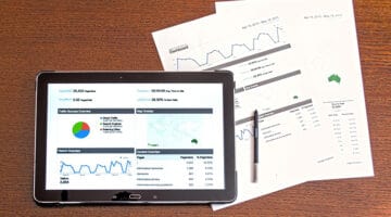 A tablet screen and hard copies of document showing business graph statistics