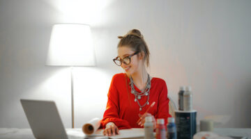 woman wearing red long sleeved top working from home – looking at her computer