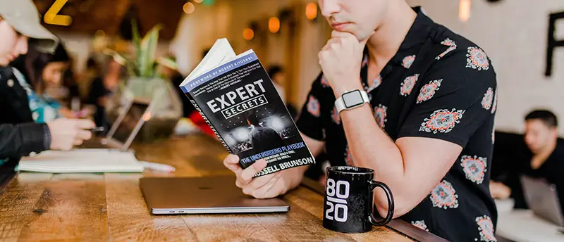 A man in black polo reading a book about experts