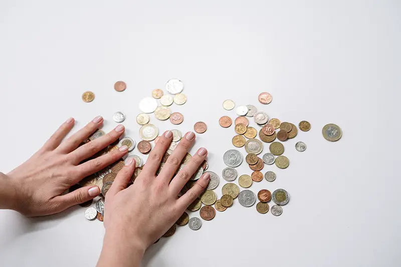 Person with their hands covering a pile of coins spread out on white surface