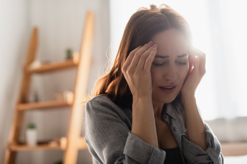 brunette woman with closed eyes suffering from pain and touching head at home