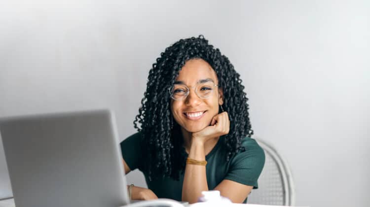 happy ethnic female student sitting at a table with laptop
