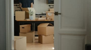man in black tshirt standing next to brown cardbox boxes in an office