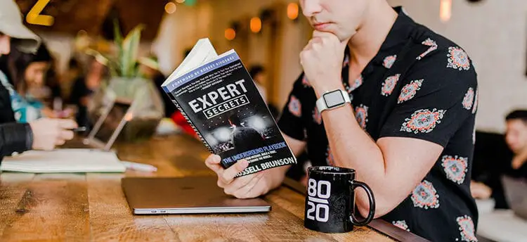 A person in black reading a book and black coffee mug beside him