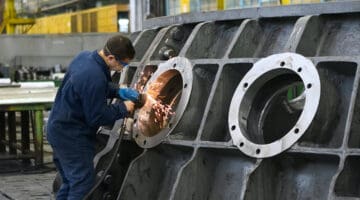 man welding round window frame in manufacturing company
